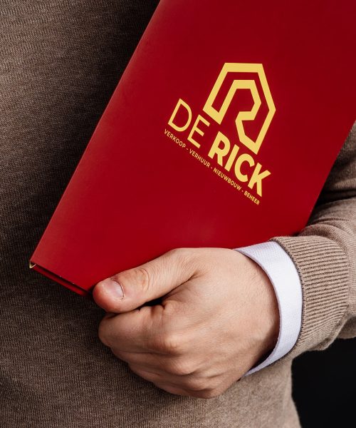 Iemand die een rode map van Immo De Rick vasthoudt, dat vastgoedbeheer aanbiedt